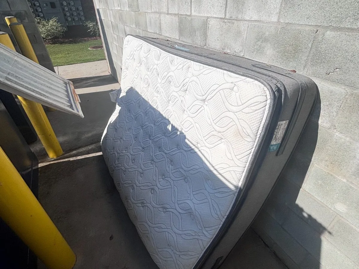Mattress and box spring dumped against the wall of a commercial dumpster enclosure